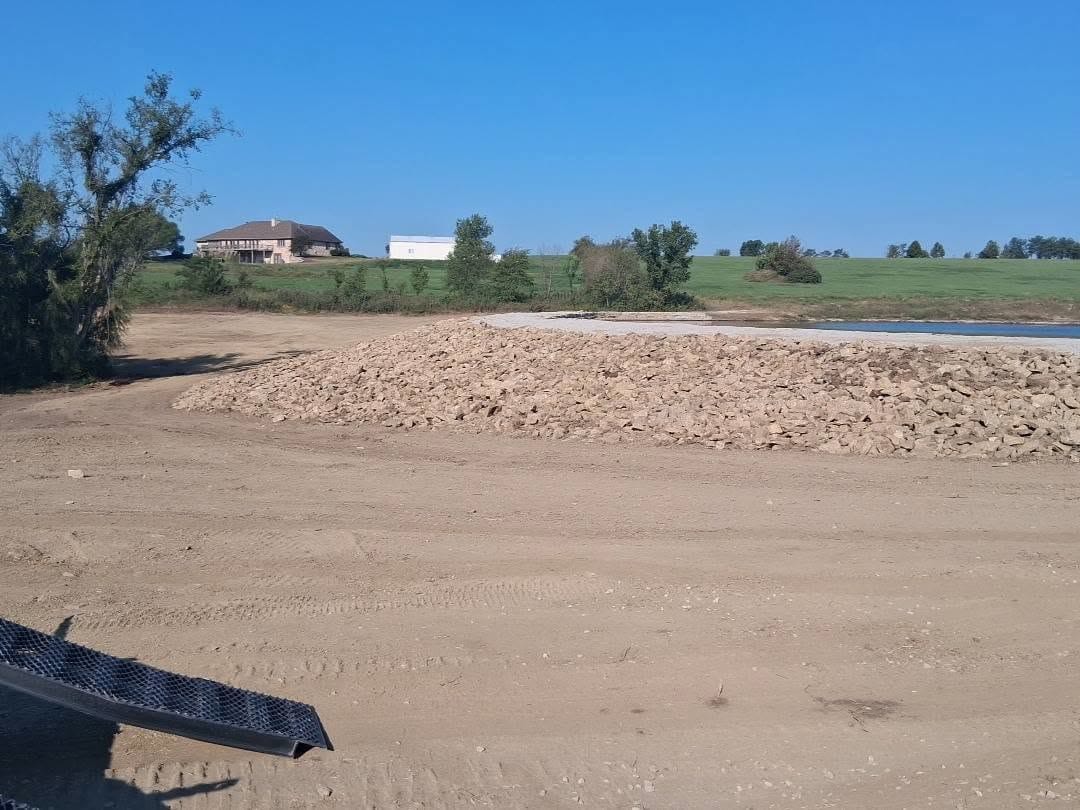 Load of shoreline rock staged beside a pond before placement