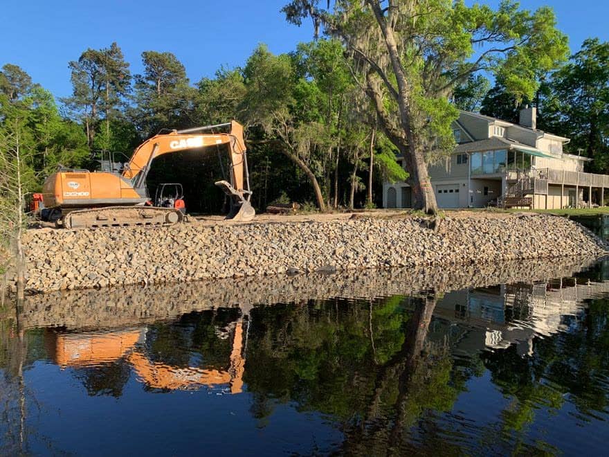 Excavator placing rock riprap along a lake shoreline